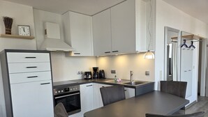 A modern kitchen with white cabinets, a built-in oven, a coffee maker, and a dining area with a table and chairs. - Duhner Düne apartment 25, WLAN, elevator, roof terrace, close to the beach, non-smoking (Cuxhaven)