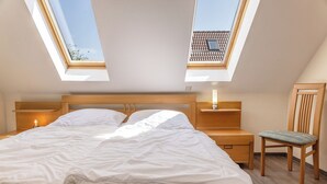 Un dormitorio con tragaluz, una cama, una mesita de noche, una silla y un buró.