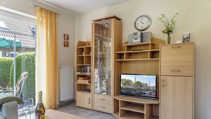 Un salón con un mueble de televisión de madera, una vitrina de vidrio y una mesa de comedor con una botella y vasos.