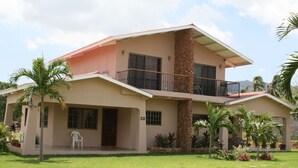 A two-story house with a balcony, a stone pillar, and a well-maintained lawn. - Beautiful Two Bedroom In Gated Community SPECIAL RATES FOR MONTHLY! (El Pajonal)