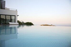 Relax by the serene pool, surrounded by lush views of a distant island.
