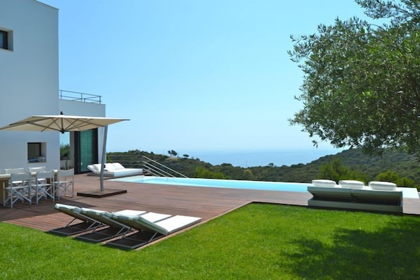 Enjoy a serene ocean view from the deck, featuring a pool, lounge chairs, and dining area.