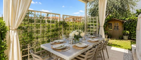 An outdoor dining area with a table set for four, surrounded by chairs, under a covered patio.