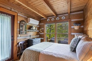Cozy bedroom with a large bed, wooden desk, and a window offering a view of the surrounding trees.
