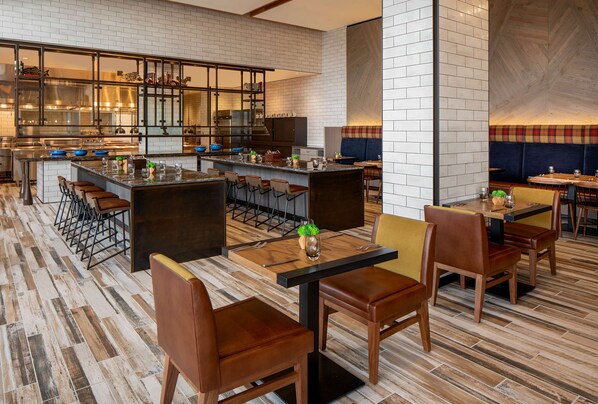 A modern restaurant with a bar area, high chairs, and a kitchen in the background.