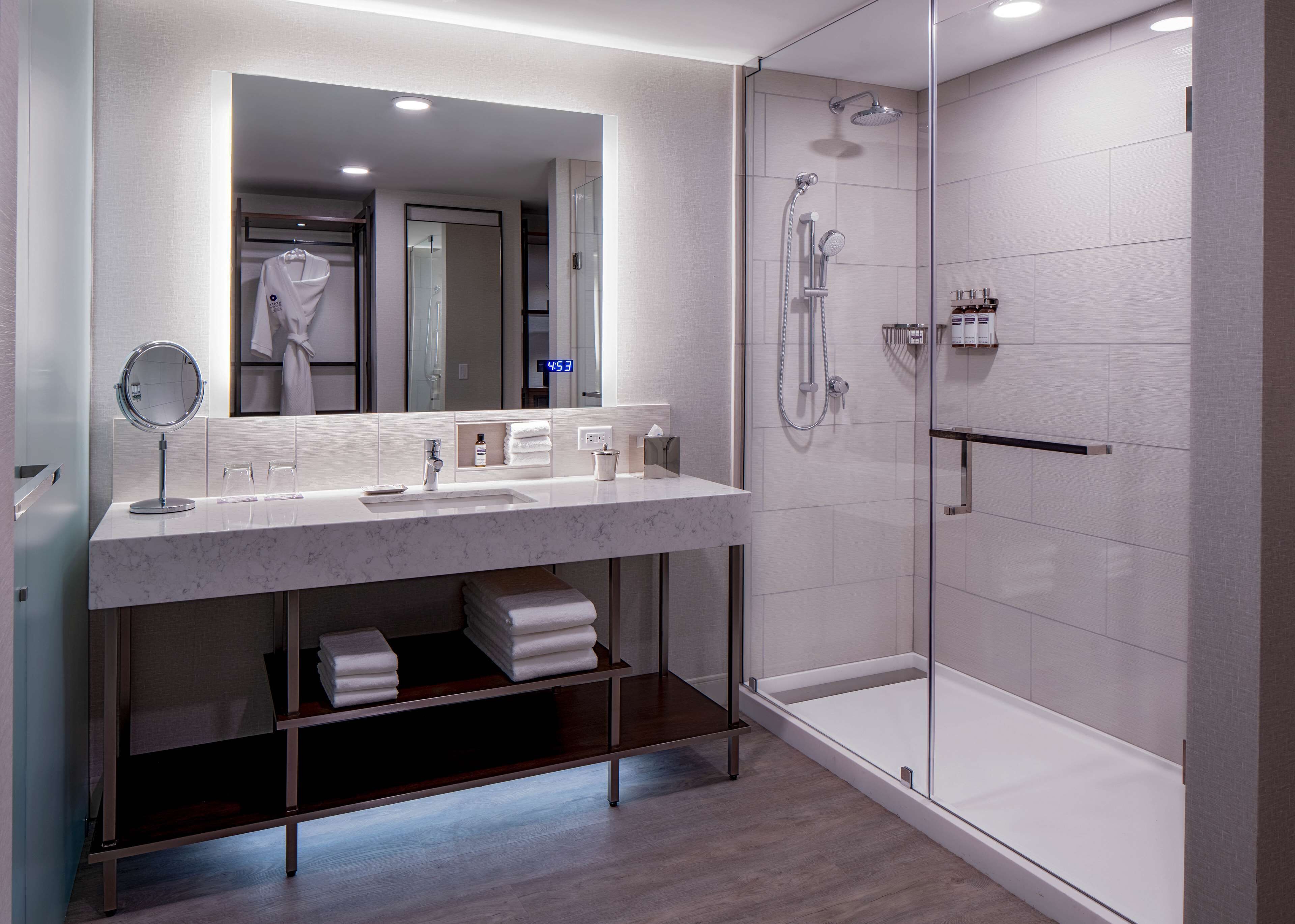 Een moderne badkamer met een marmeren wastafel, een ronde spiegel, een douche met glazen wand en netjes opgevouwen handdoeken.