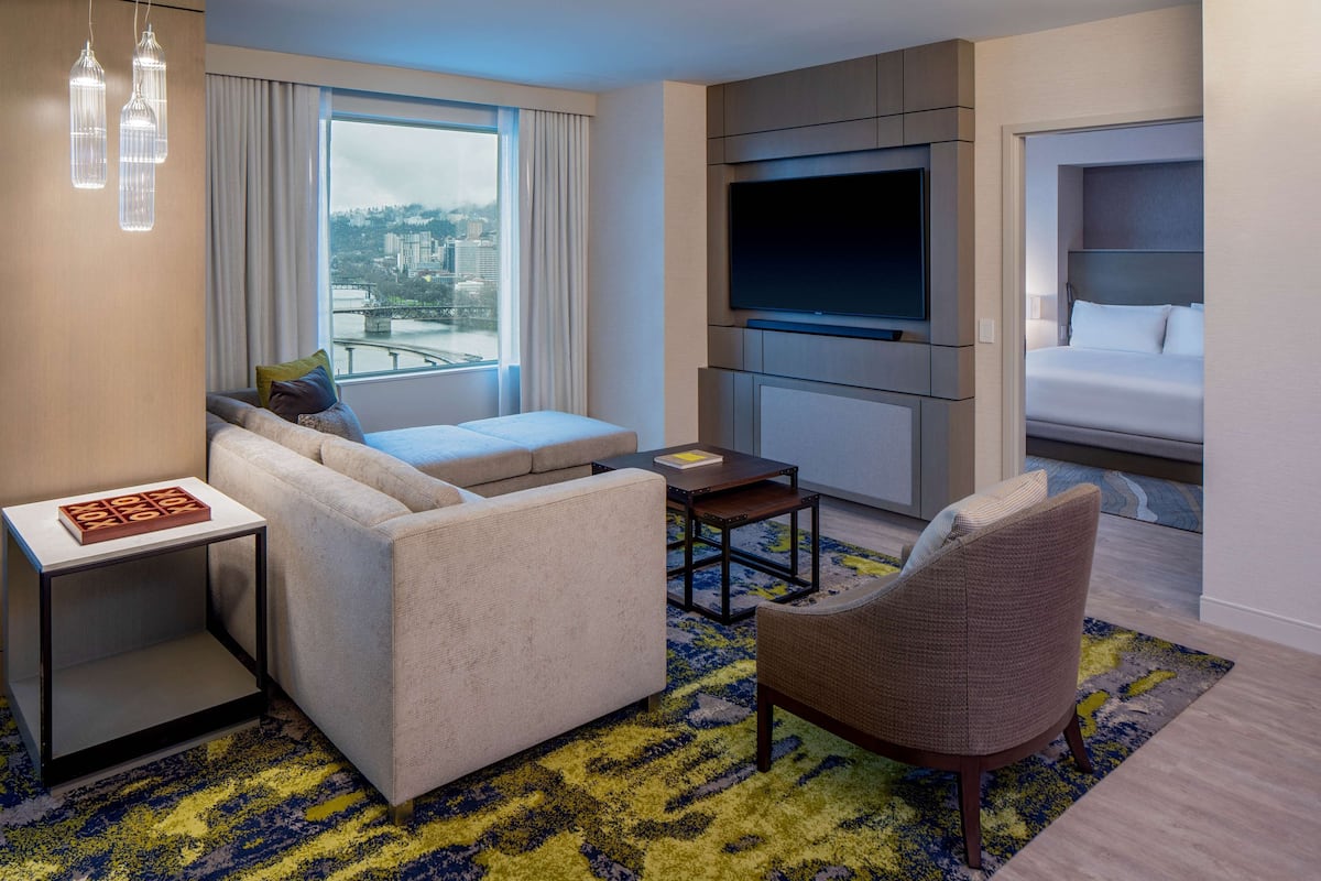 A modern hotel room with a sofa, armchair, small table, and a TV.