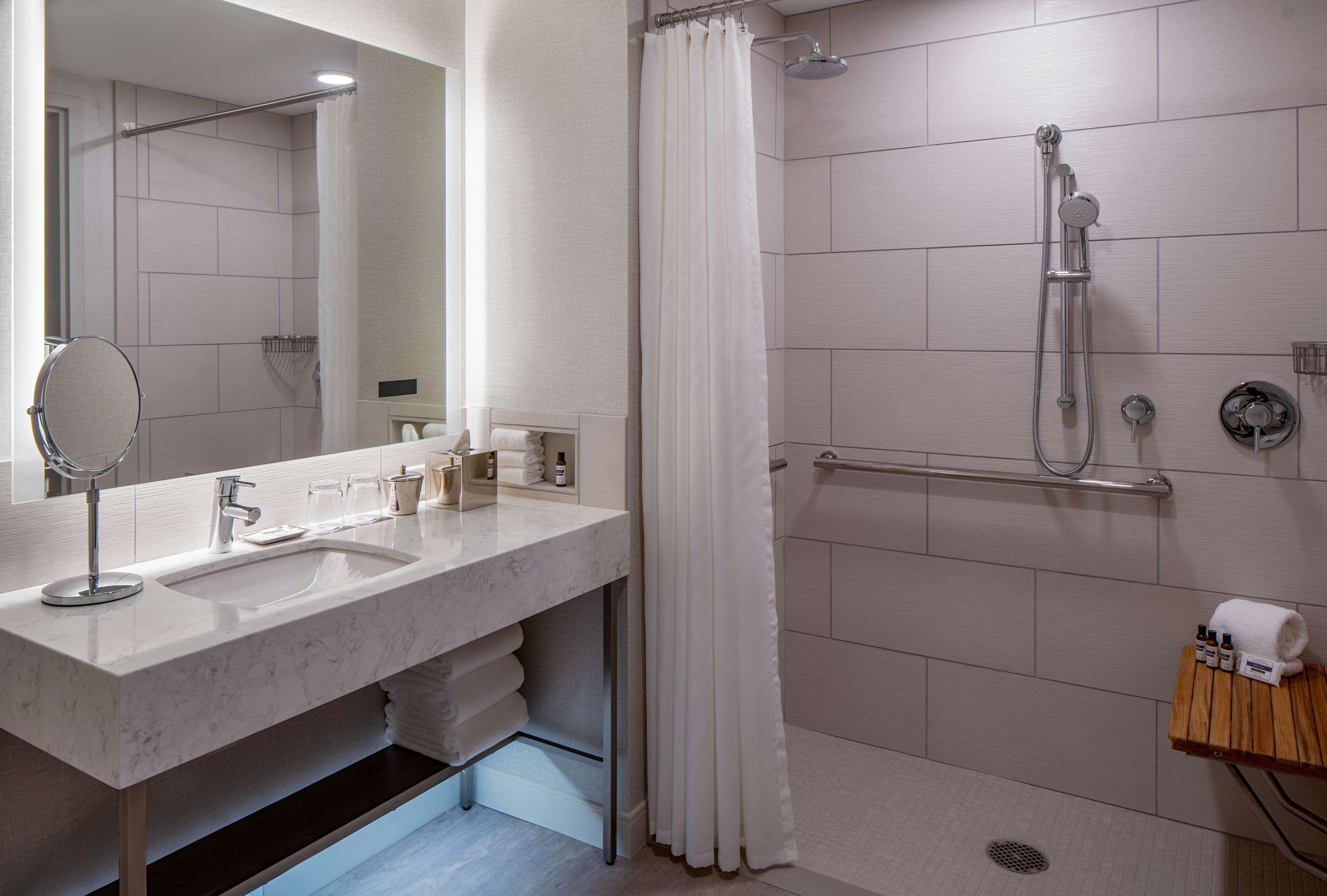 A modern bathroom with a double sink, a shower with a handheld showerhead, a towel rack, and a mirror.