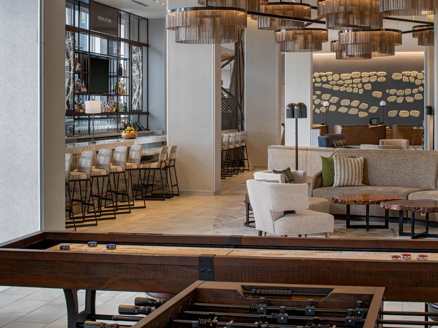 A modern bar area with stools, a foosball table, and a bar counter with a variety of bottles.