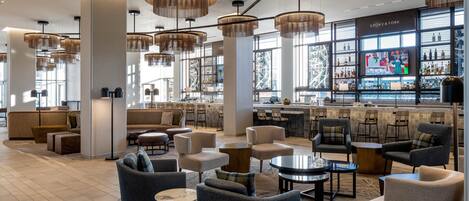 A modern bar area with seating, large windows, and a television screen displaying a Christmas scene.