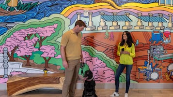 A man and woman standing in front of a colorful mural with a dog.