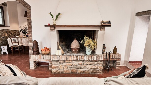 A cozy living room with a stone fireplace, a dining area with a table and chairs, and a large cushioned sofa. - Podere Piaggette of segalgari - Sea side  (castagneto carducci)