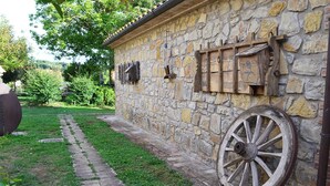 Un bâtiment en pierre à l’aspect rustique, une roue de charrette en bois et un chemin qui y mène.
