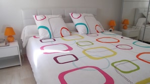 Un lit bien fait, recouvert d’une couvre-lit aux motifs géométriques colorés, avec des oreillers blancs et deux lampes de chevet.
