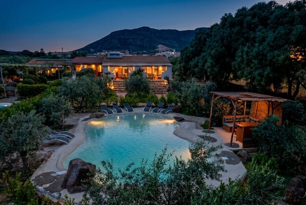 A pool with lounge chairs, a wooden deck, and a building with steps leading up to it.