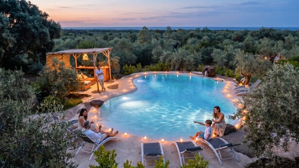 A pool with lounge chairs and a wooden structure with lights.