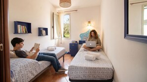 A small, cozy room with two beds, a desk, and a bookshelf.