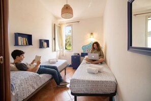 A small, cozy room with two beds, a desk, and a bookshelf.
