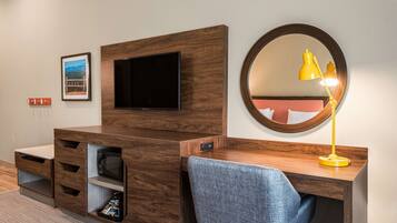 A modern room with a wooden desk, a television mounted on the wall, a round mirror, and a small shelf with a television.