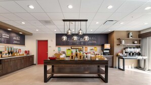 A modern cafe with a central table, a chalkboard menu, and various coffee machines. - Hampton Inn Batesville (Batesville)