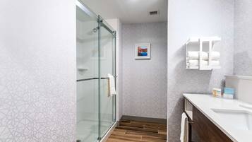 A modern bathroom with a glass shower enclosure, a wooden floor, a white sink, and a towel rack.