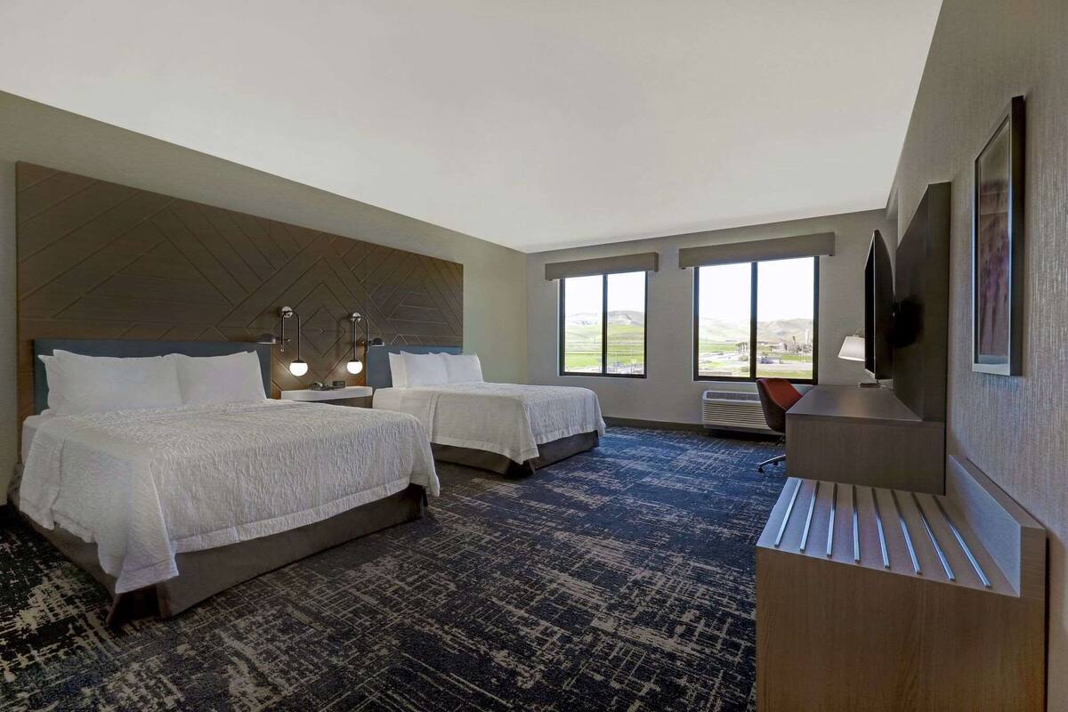 A hotel room with two beds, a desk, a chair, and a TV.