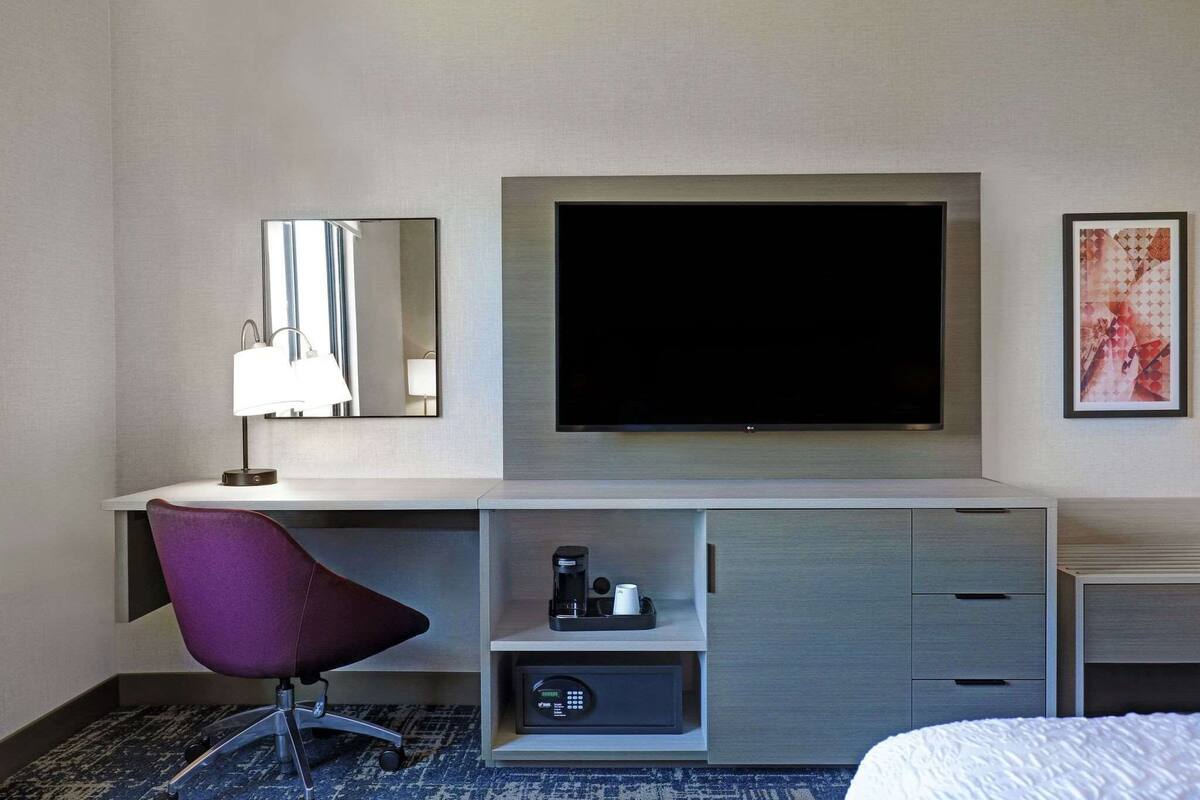 A hotel room with a flat-screen TV, a desk with a chair, a coffee maker, and a bed.