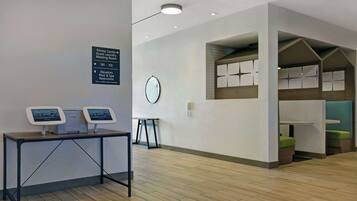 A hotel lobby with a reception desk, a sign indicating the fitness center, guest laundry, and meeting room, and a small table with a clock.