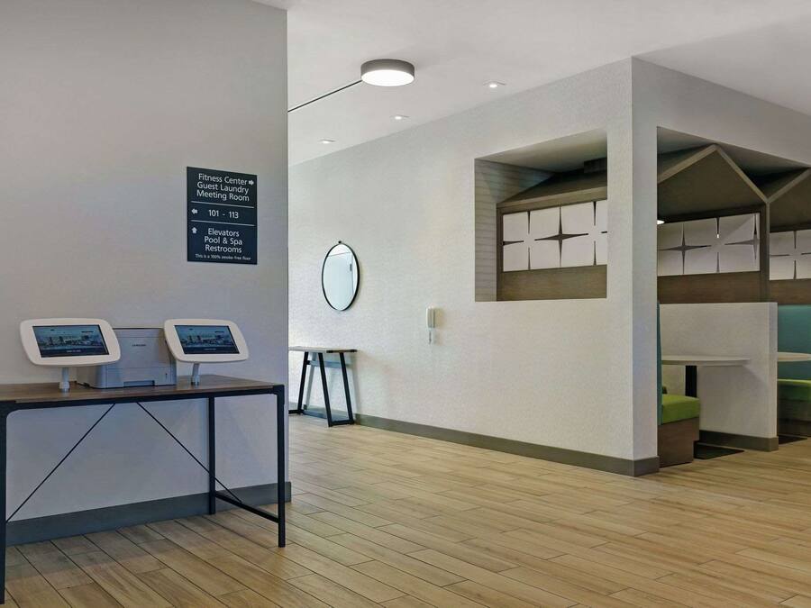A hotel lobby with a reception desk, a sign indicating the fitness center, guest laundry, and meeting room, and a small table with a clock.