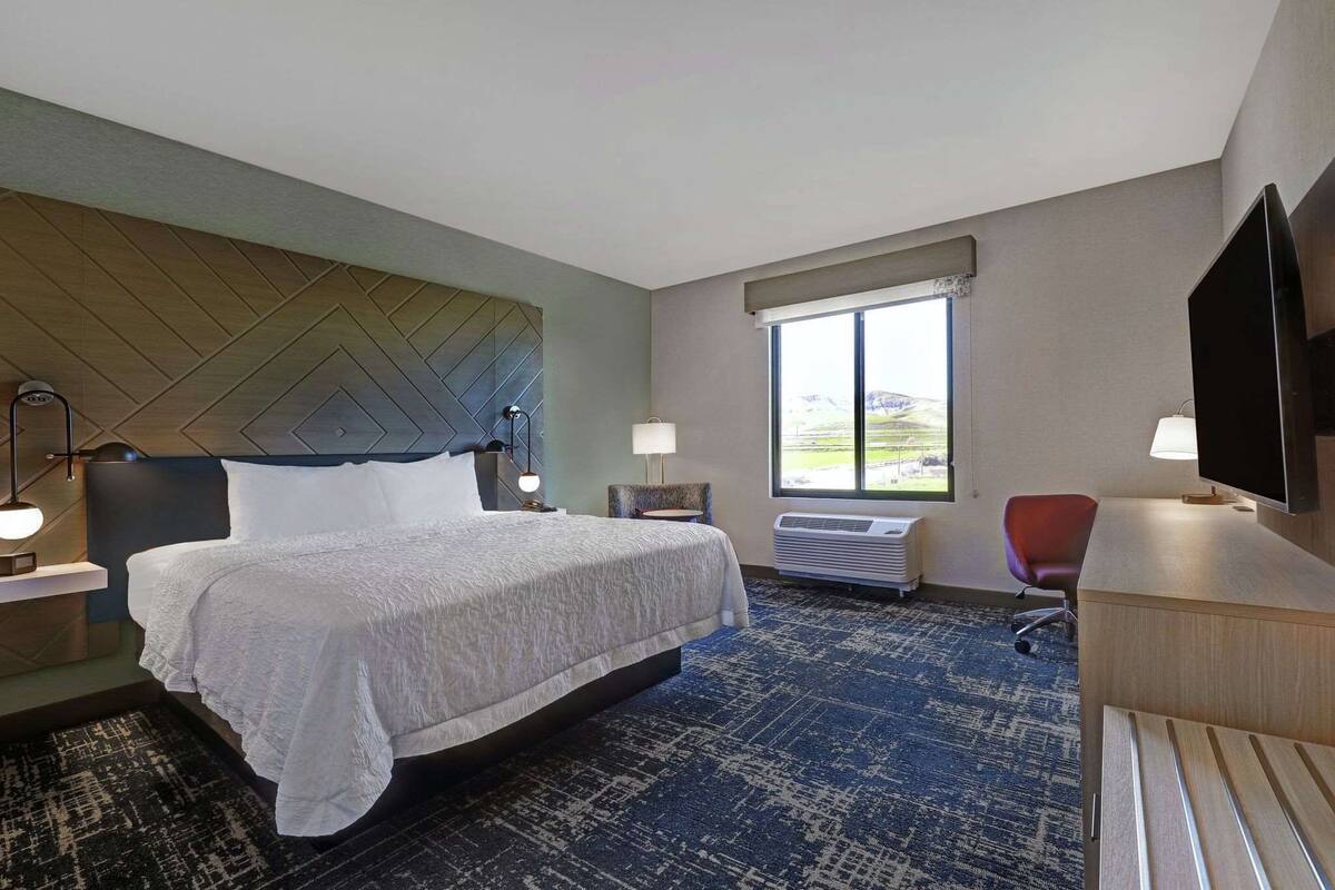 A hotel room with a bed, a desk, a chair, a TV, a window, and a view of the outdoors.