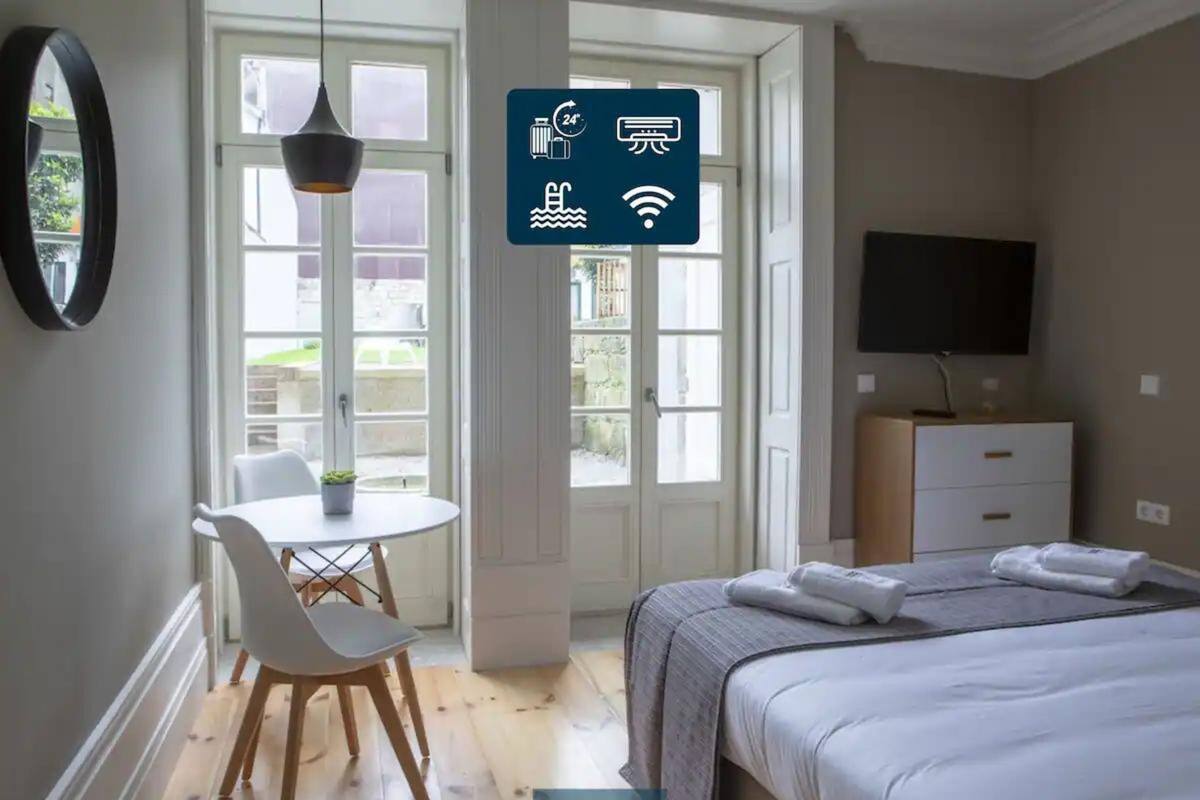 Egy modern hálószoba, amelyben található egy ágy, egy éjjeliszemély, egy televízió, és nagy ablakokon keresztül kilátás nyílik a szabadba.