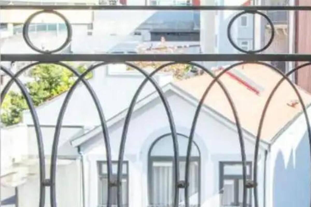 Egy fehér homlokzatú épület, melynek egy fém korláttal ellátott erkélye van.