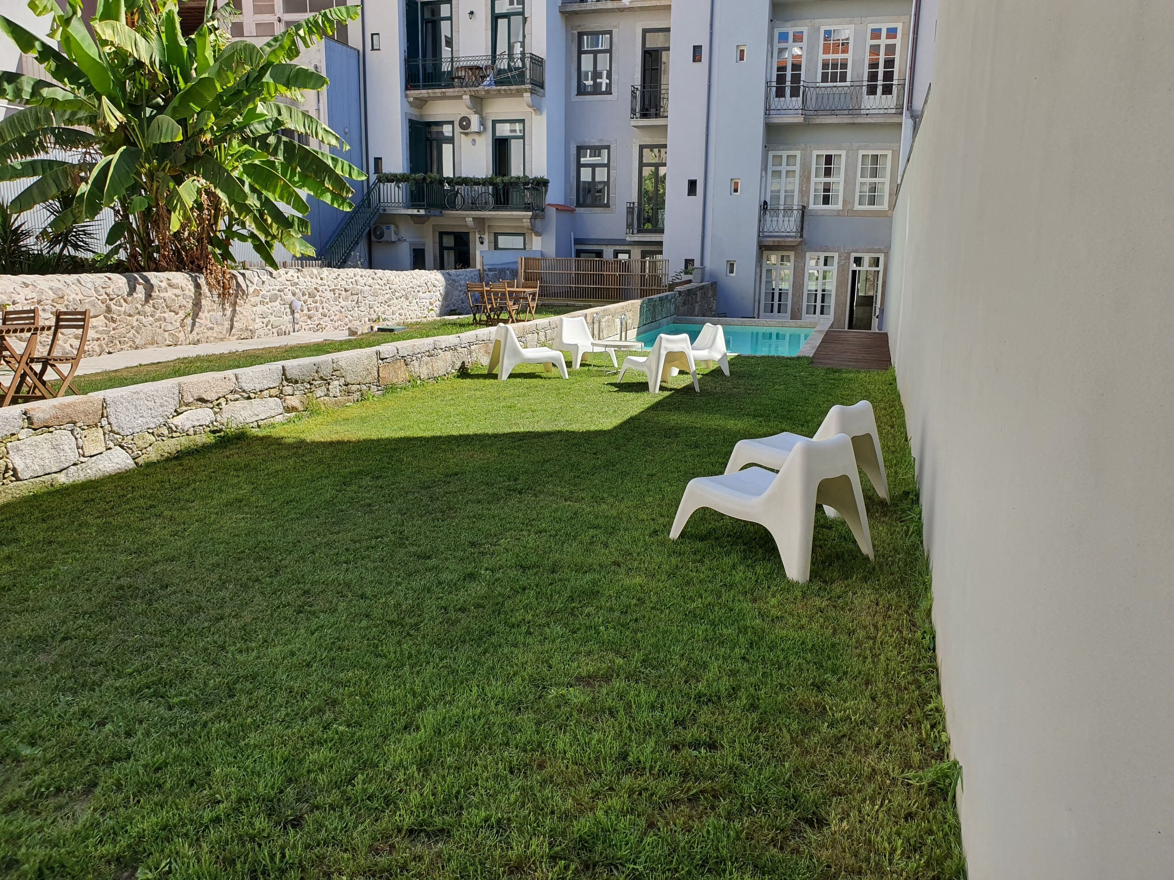 Un espacio al aire libre con césped cuidado, sillas de plástico blancas y un muro de piedra.