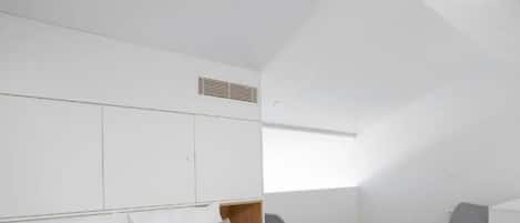 Habitación de hotel moderna con una cama grande, dos sillas, una mesita y un ventanal que deja entrar luz natural.