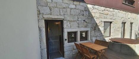 Un bâtiment en pierre doté d’une terrasse en bois, d’une table et de chaises.
