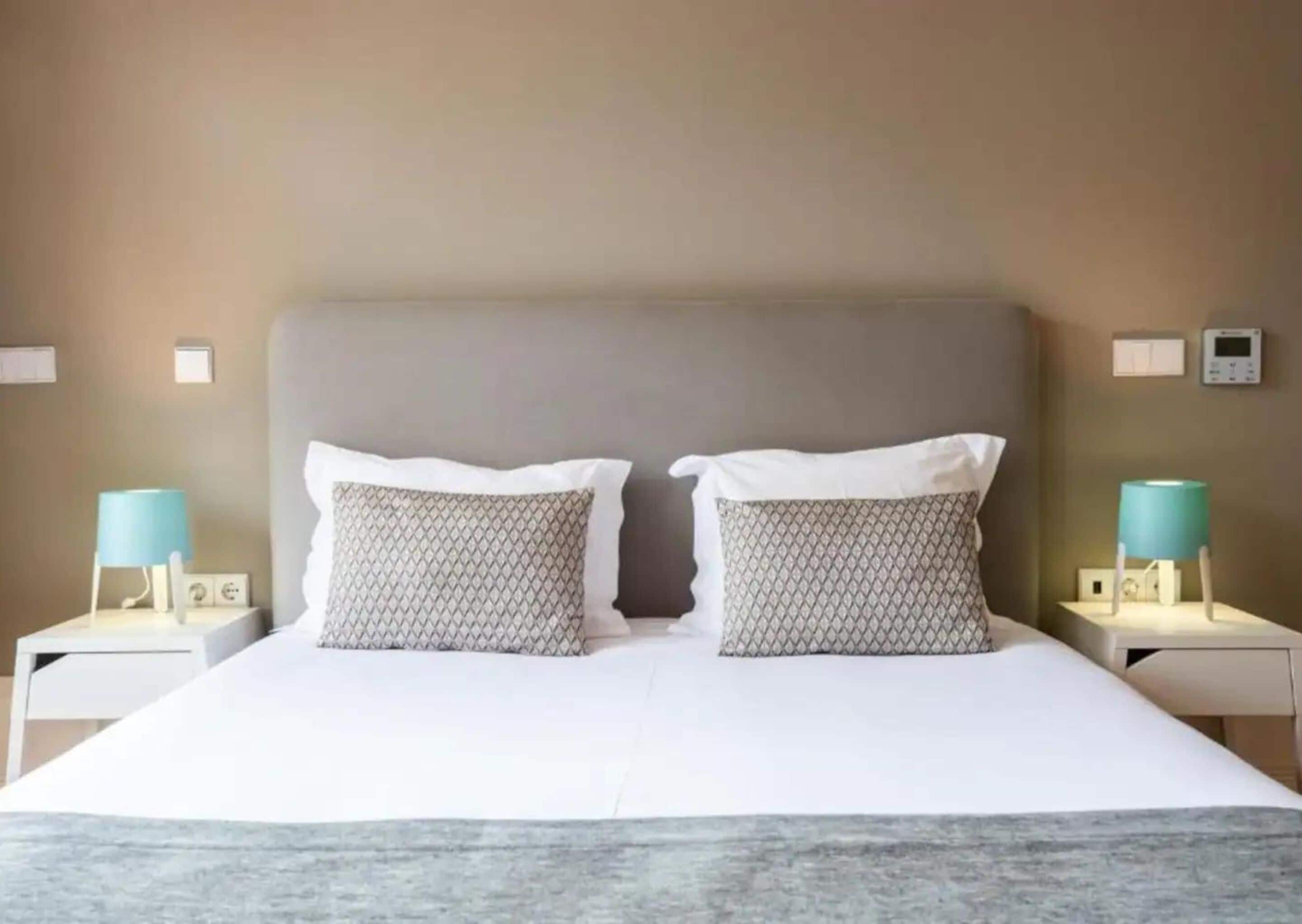A hotel room with a large bed, two bedside tables with lamps, and a plain wall.