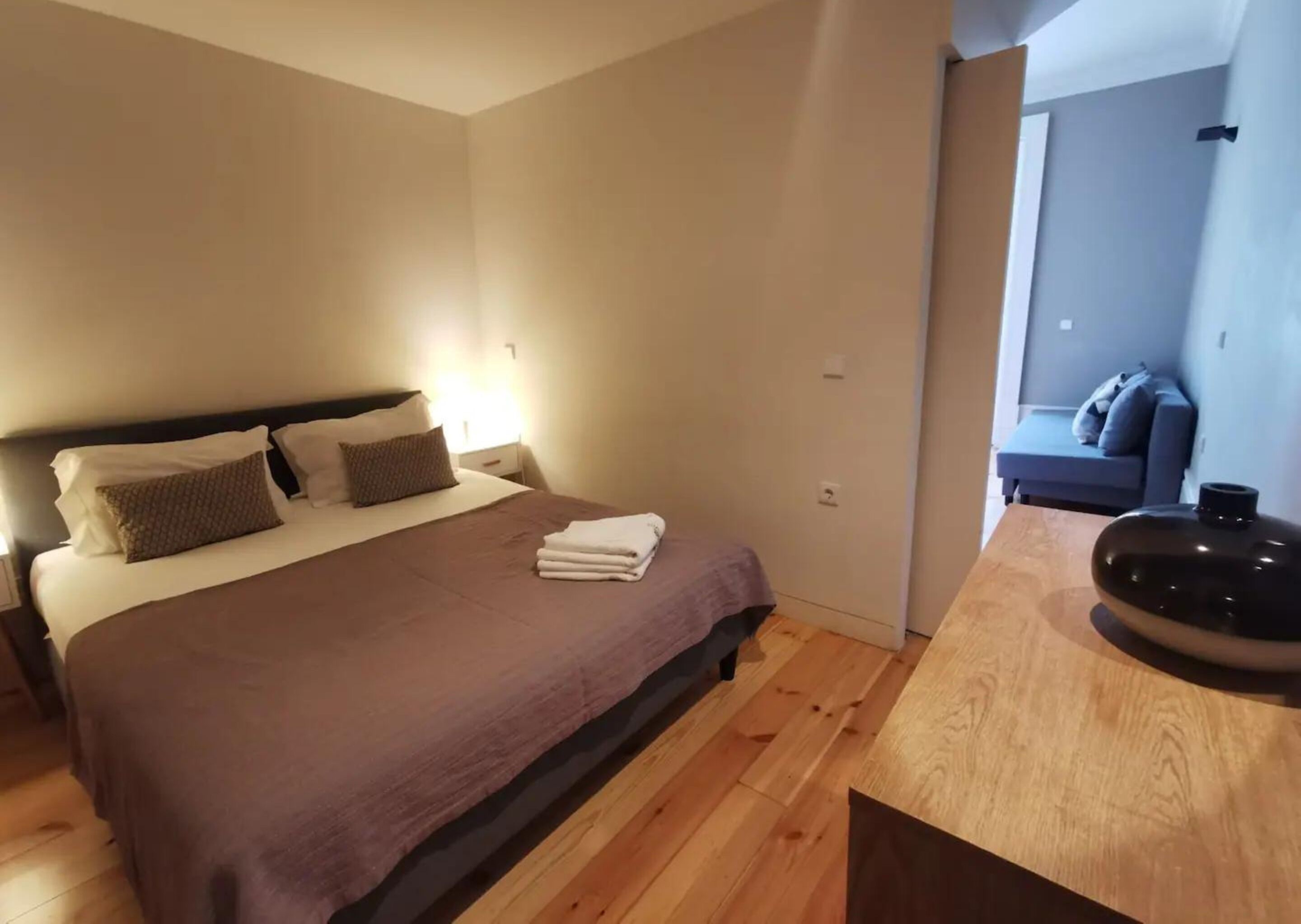 Habitación de hotel con cama, mesita de noche y vista a un área de estar.