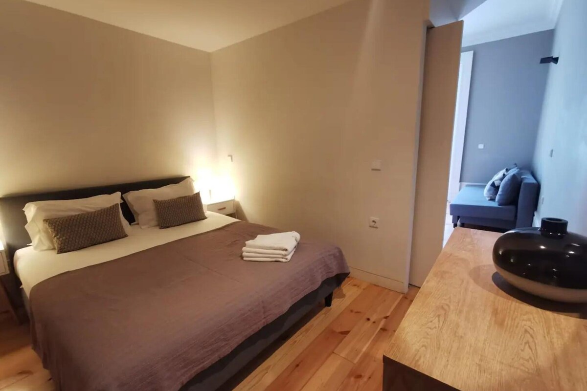 Hotellihuone, jossa on sänky, yöpöytä ja näkymä oleskelutilaan.