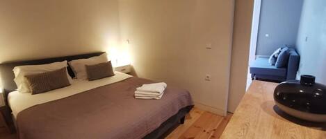 A hotel room with a bed, a bedside table, and a view of a living area.