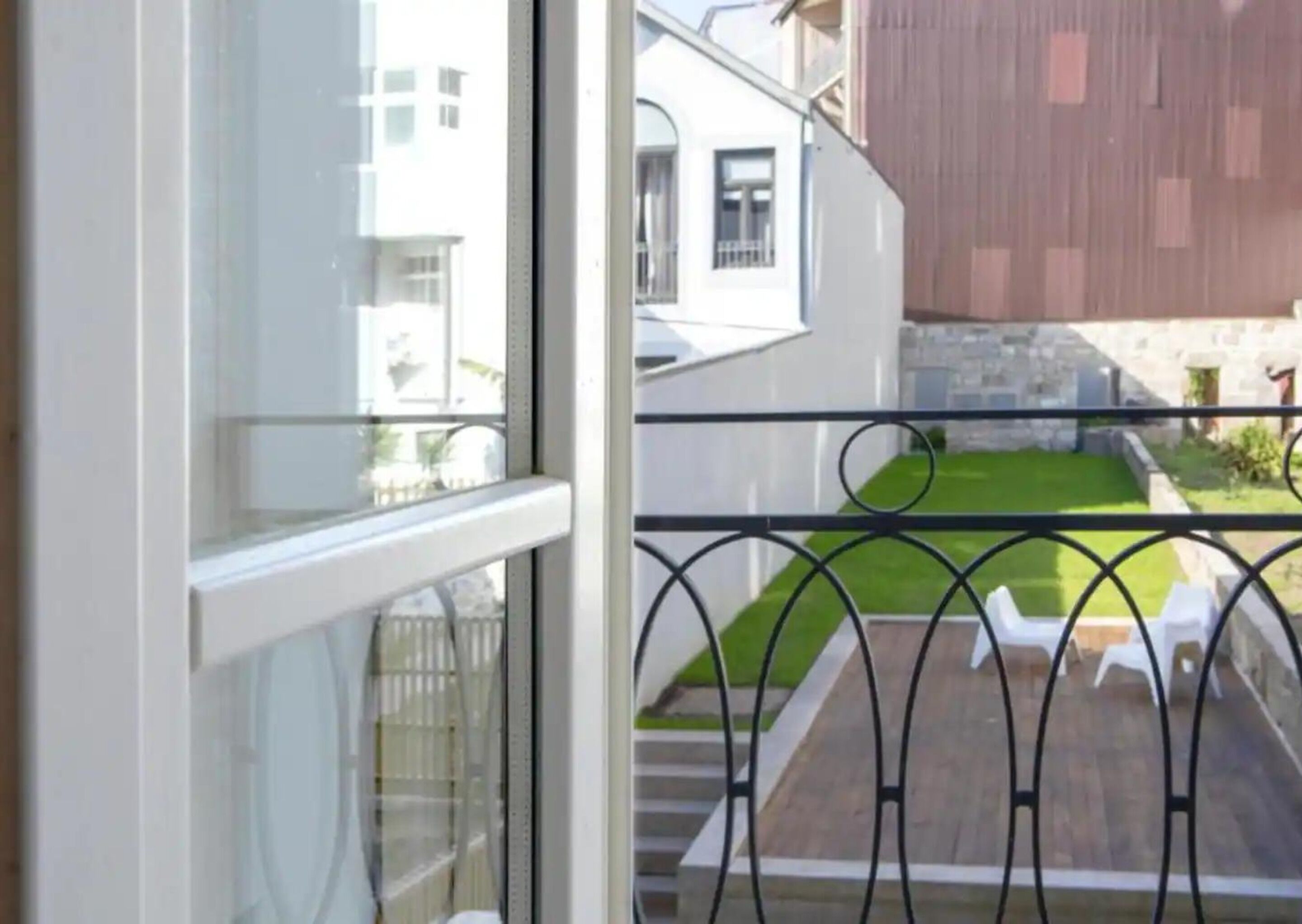 A balcony with a metal railing, a grassy area, and a view of a building with a stone wall and a wooden structure.
