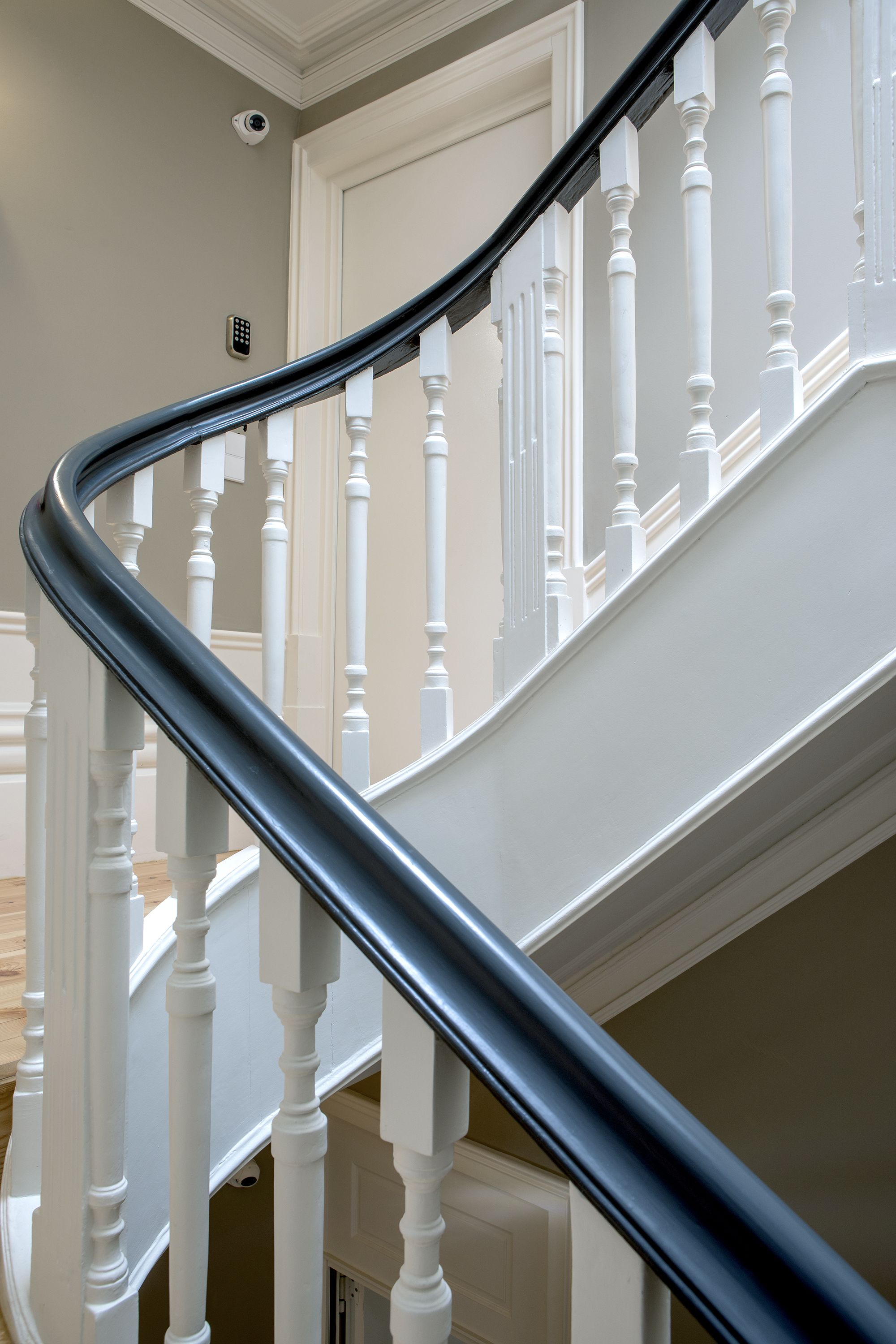 Una escalera curva con balaustres blancos y barandilla negra.