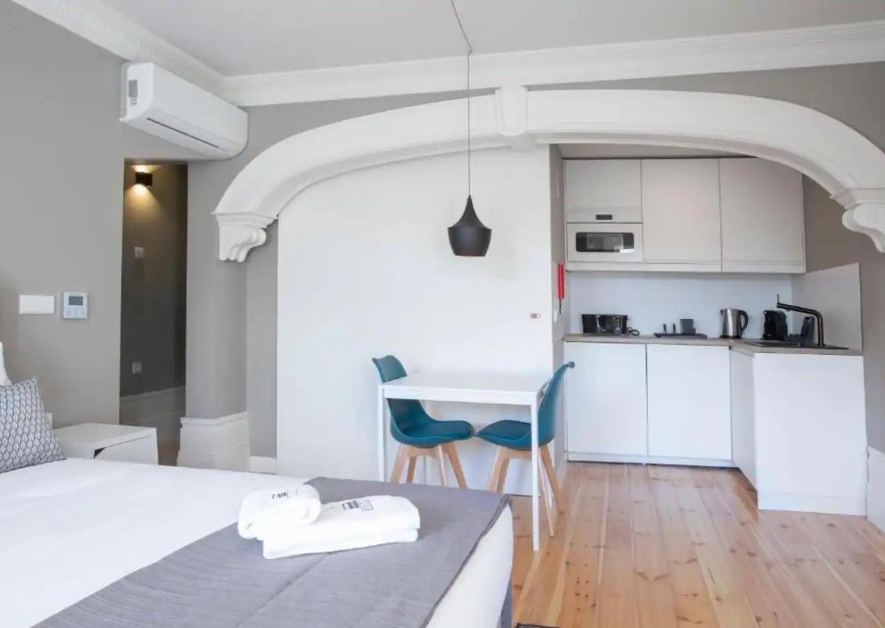 A modern hotel room with a bed, a desk, and a kitchenette.