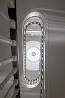 Vista a través de una ventana con diseño circular, una escalera con barandillas blancas y un marco metálico.