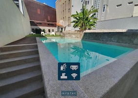Una piscina con borde de piedra, escalones de acceso y vistas de edificios circundantes.