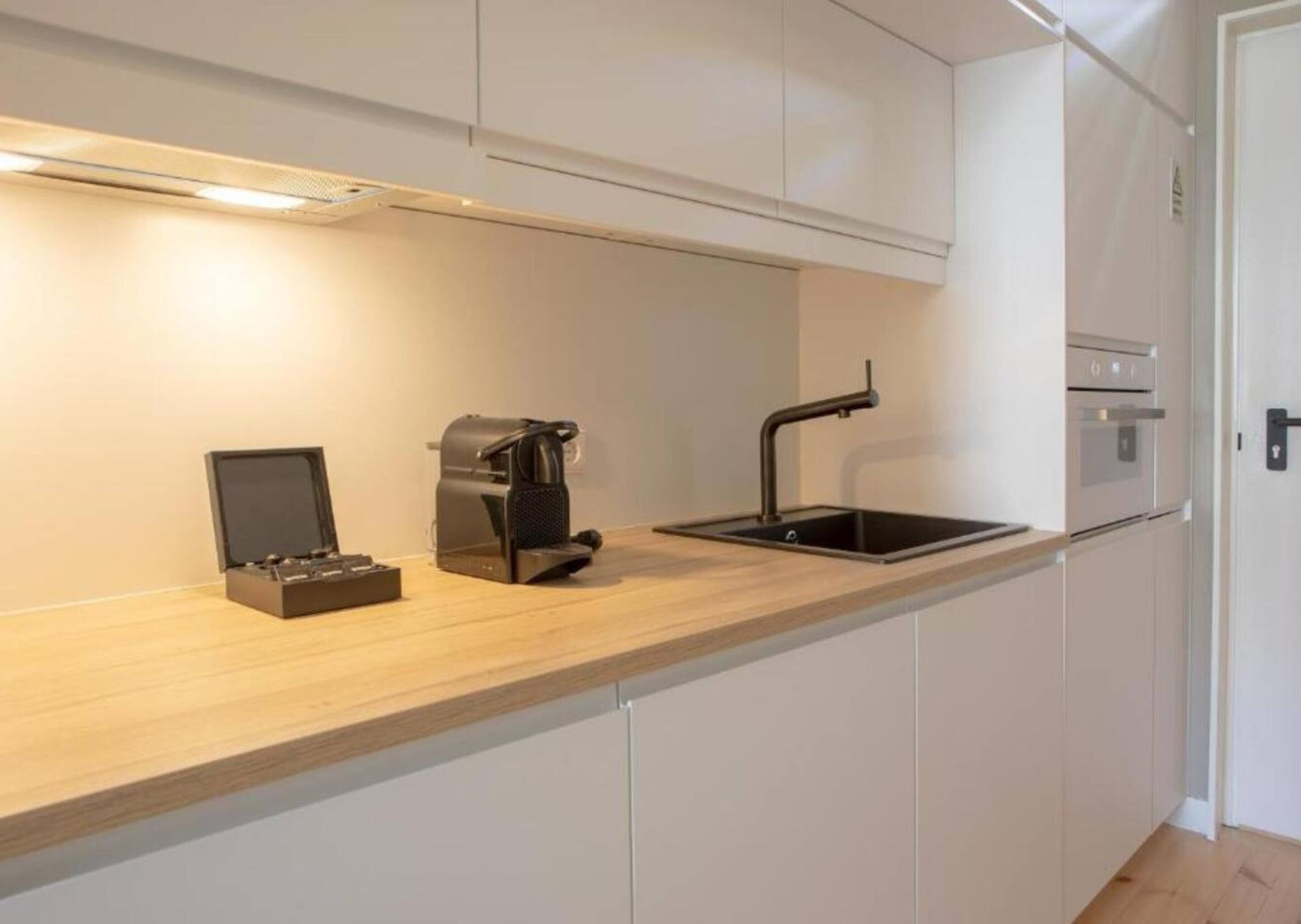 A modern kitchen with a wooden countertop, a coffee machine, a sink, and built-in cabinets.