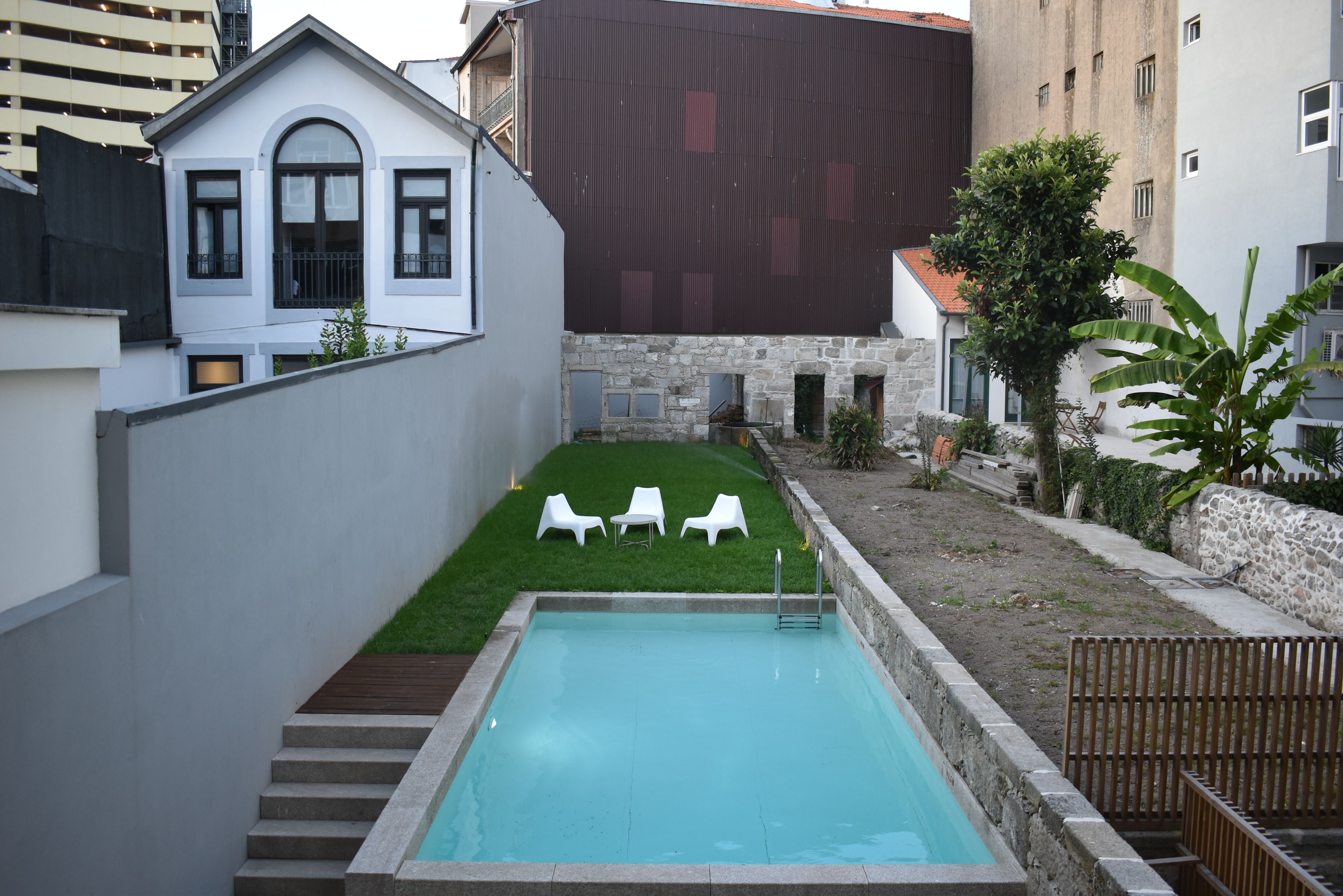 Una piscina con gradini che conducono all'acqua, circondata da un muro in pietra e da una zona verde con lettini bianchi.