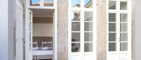 Una habitación pequeña y privada con cama, dos ventanas y una puerta.