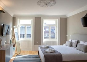 Un dormitorio con cama, dos ventanas, televisor y espejo.