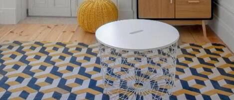 Una habitación con un ventanal grande, un televisor de pantalla plana en la pared, una mesa redonda blanca y un suelo con diseño.