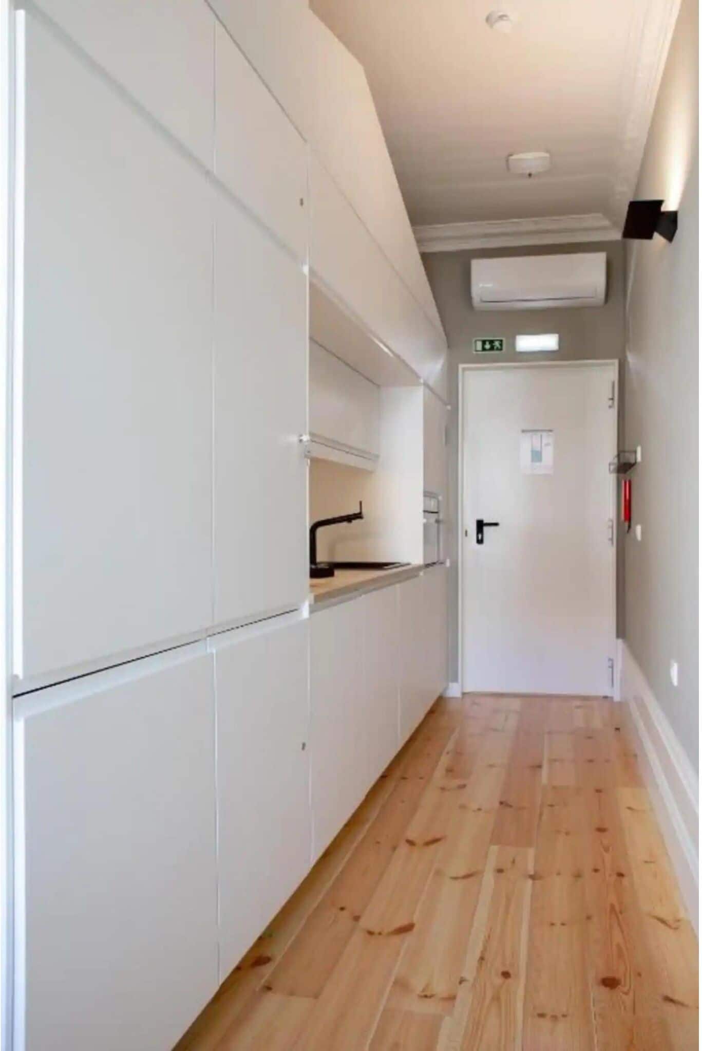 A narrow hallway with white cabinets, a wooden floor, and a door at the end.